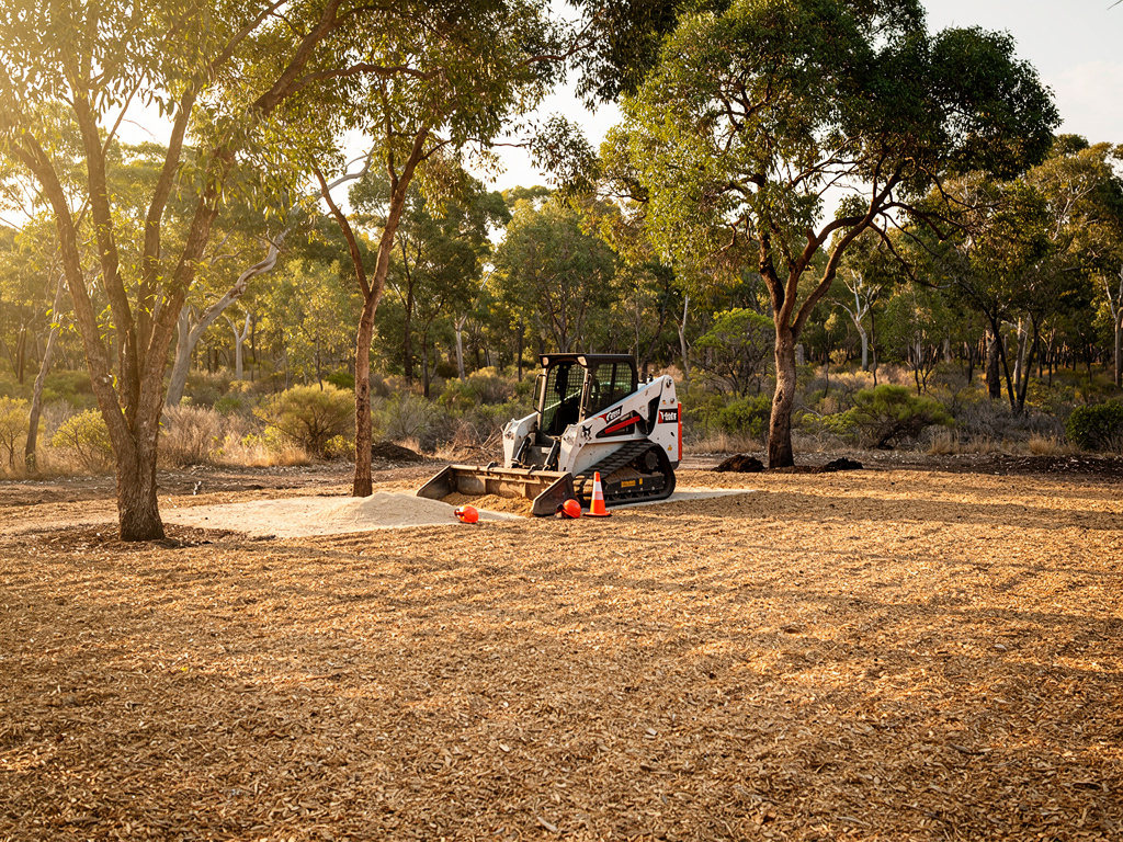 A wide view of a freshly mulched clearing with an even layer of wood mulch under scattered mature trees.